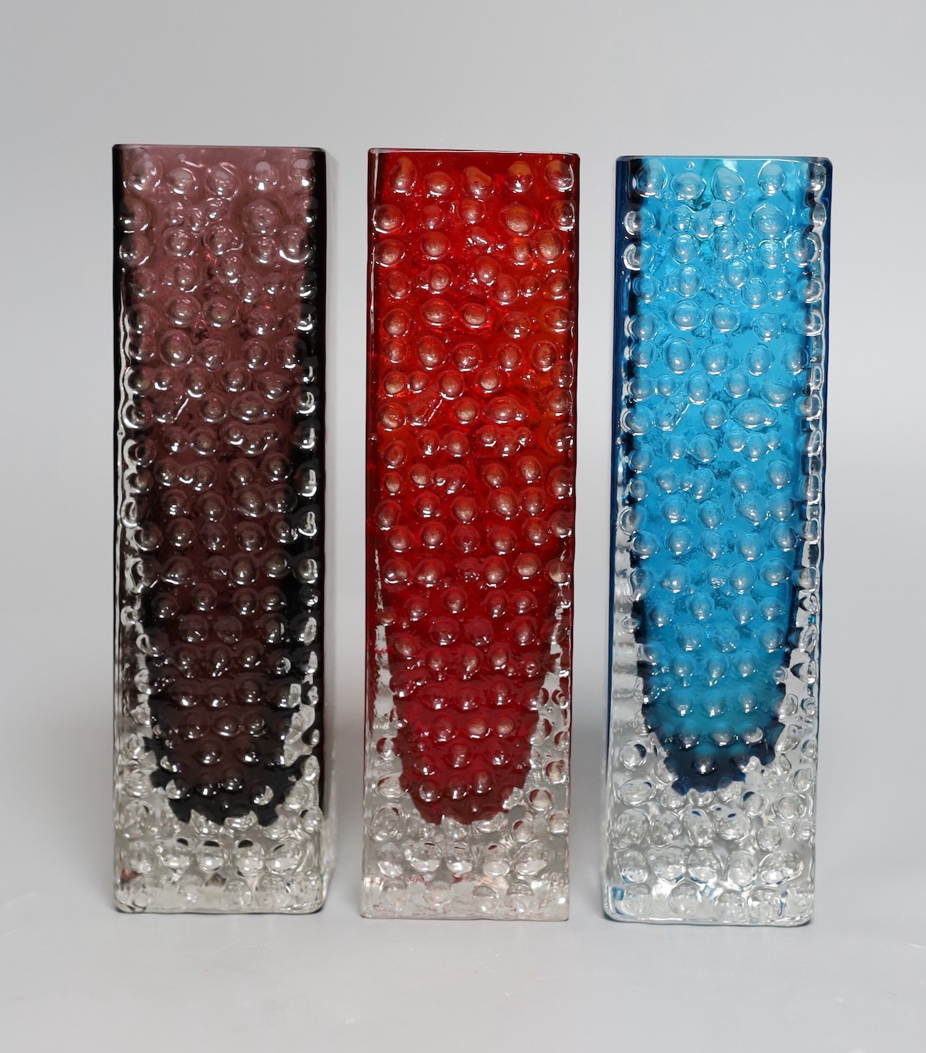 A trio of Whitefriars 'Nailhead' vases, designed by Geoffrey Baxter, kingfisher blue, red and amethyst glass, 20 cms high